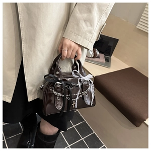 Detail of dark brown patent leather handbag with lace bows and silver cross chains
