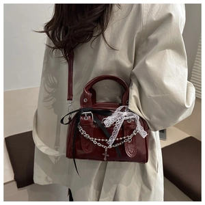 Detail of dark red glossy bag with silver chains, cross charm and lace bow accents