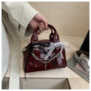 Detail of burgundy patent leather handbag featuring lace bows and gothic metal cross chain