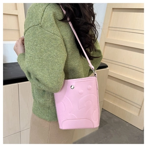 Détail du sac seau rose à motifs embossés porté avec un pull en maille vert pastel