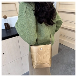Détail du sac seau doré avec texture embossée et fermoir magnétique circulaire élégant