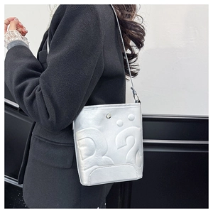 Sac seau argenté avec lettrage gaufré, porté à l'épaule sur un manteau noir élégant