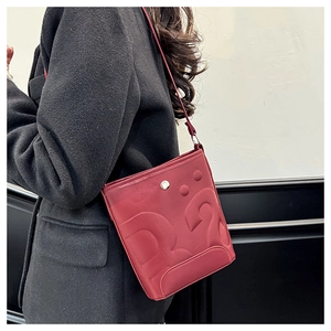 Détail du sac seau rouge mat avec texture logo embossée et boucle en métal argenté