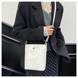 Gros plan d'un sac seau blanc gaufré avec motif abstrait et fermoir métallique sur modèle