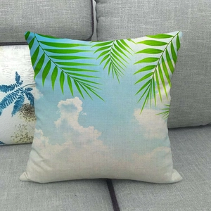 Detail of tropical palm leaf and blue sky print on linen cushion cover on grey sofa
