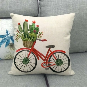 Close-up of linen pillowcase with watercolor red bicycle and cactus pattern on grey sofa