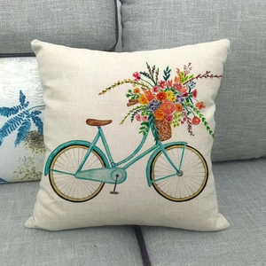 Linen pillow cover with watercolor bicycle and floral print on a gray fabric sofa