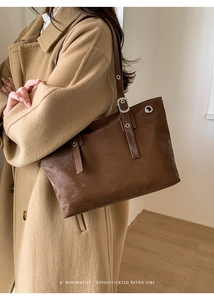 Detail of dark brown leather tote bag with silver eyelets on a khaki wool coat