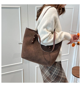 Detail of a large brown suede tote bag with leather straps and gold rivets on a model