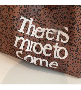 Close-up of leopard print tote bag with white There is more to come text on woven canvas