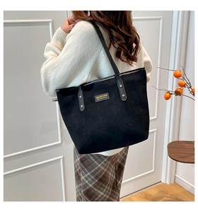 Detail of matte suede black tote bag with gold logo text and leather rivet straps