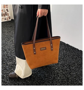 Detail view of brown faux suede tote bag featuring a leather logo patch and metal rivets