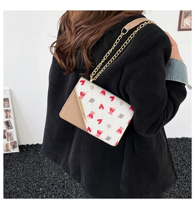 Detailed view of women's shoulder bag featuring red heart patterns and gold chain strap