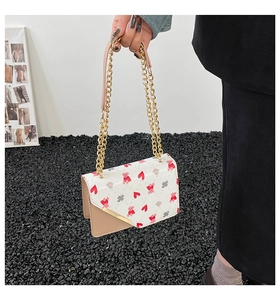 Detail of a beige flap bag with red hearts, pink bear prints and a gold chain strap