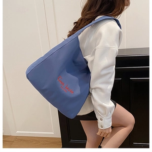 Close-up of blue canvas tote bag with red 'C'est lavie' embroidery and large shoulder strap