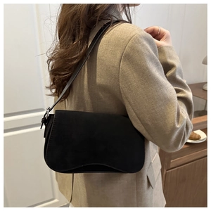 Detail of a black matte suede shoulder bag shown on a model in a cozy indoor setting