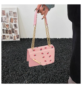 Detail of pink strawberry print square bag featuring gold chain strap and metal trim