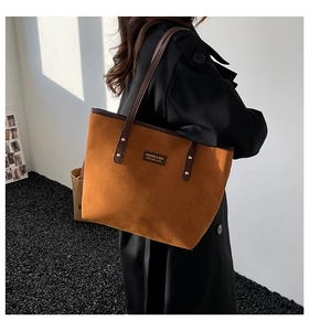 Detalle de bolso tote de ante marrón con asas de cuero y remaches metálicos dorados