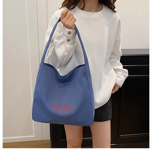 Close-up of blue canvas tote bag featuring red C'est la vie embroidery on the front