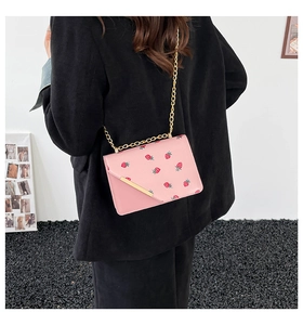 Detail of pink crossbody bag with strawberry print and gold metal chain on a model