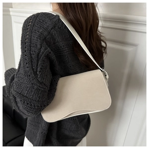 Detail of a minimalist beige shoulder bag with a curved base and narrow strap on a model