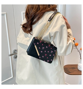 Close-up of elegant black floral crossbody bag with gold chain strap worn by a model