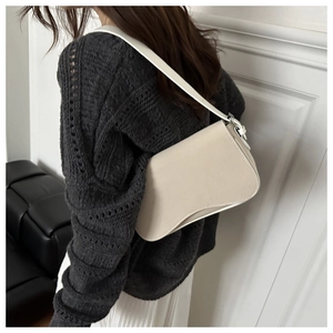 Detail shot of a beige leather saddle shoulder bag showing the unique curved silhouette