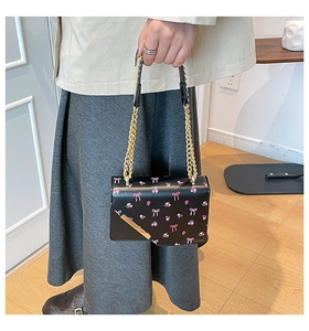 Close-up of a black floral handbag with pink bow patterns and a golden chain strap