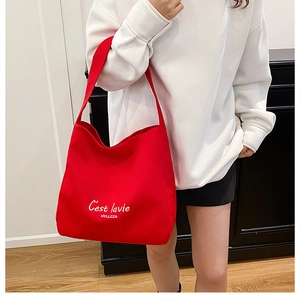 Detail of red canvas tote bag featuring C'est la vie cursive text and shoulder strap