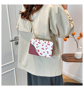 Detail of cherry print crossbody bag with gold chain strap on a trench coat model