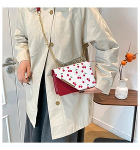 Detail showing the red cherry pattern on a white leather flap with golden chain strap