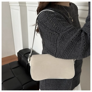Detail of cream shoulder bag with rounded base and metal buckle strap on a model