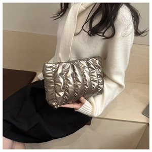 Champagne gold metallic clutch bag with pleated texture held by model against neutral wall
