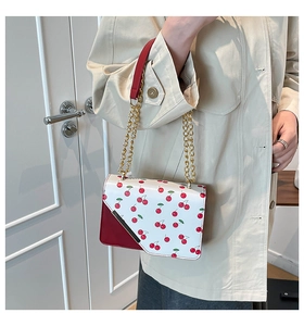 Detail of white handbag with red cherry print and gold metal chain strap for women