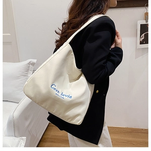 Detail of white canvas tote bag with blue C'est la vie embroidery for minimalist style