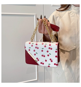 Detail of red and white cherry print handbag with gold chain handle and leather strap