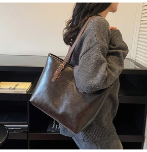 Detail view of large dark brown leather tote bag with long shoulder strap worn by model