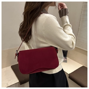 Detail view of burgundy faux suede shoulder bag with elegant wavy flap and adjustable strap