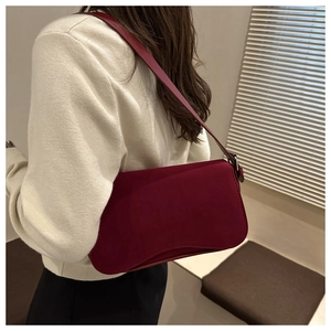 Detail of burgundy matte suede shoulder bag with silver hardware on a model