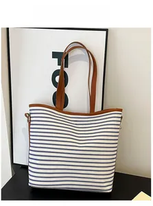 Detail of blue and white striped canvas tote bag with brown leather handles and metal rivet