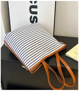 Detail of blue striped canvas tote bag showing brown leather trim and fine stitching