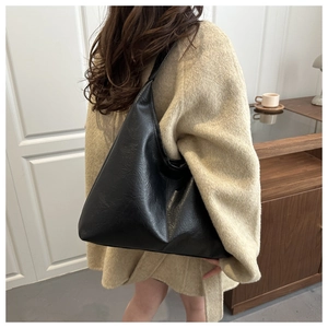 Close-up of minimalist black oversized tote bag with natural leather texture on a shoulder