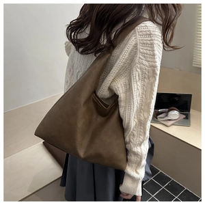 Brown faux leather hobo tote bag detail worn by model in a cozy indoor setting