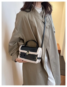 Detail view of black glossy handbag with white faux shearling trim and gold hardware