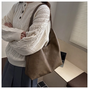 Detail of a large brown soft leather tote bag shown on model in a stylish office setting