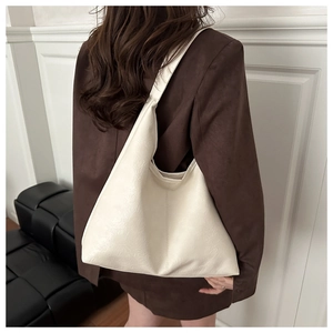 Detailed view of a white leather tote bag with soft pleats on a dark brown blazer outfit