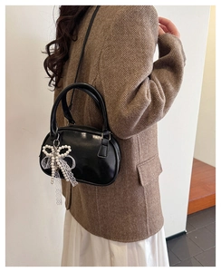 Detail of black mini crossbody bag featuring a pearl bow and white lace ribbon pendant