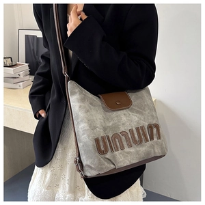 Detail of gray canvas shoulder bag with leather letter patch and magnetic flap closure