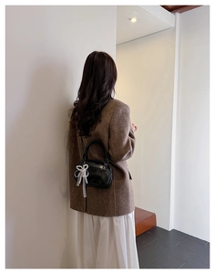 Close-up of black leather bowling bag with white lace bow detail on brown blazer
