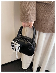 Detail of a black faux leather bowling bag featuring a pearl and lace bow charm detail